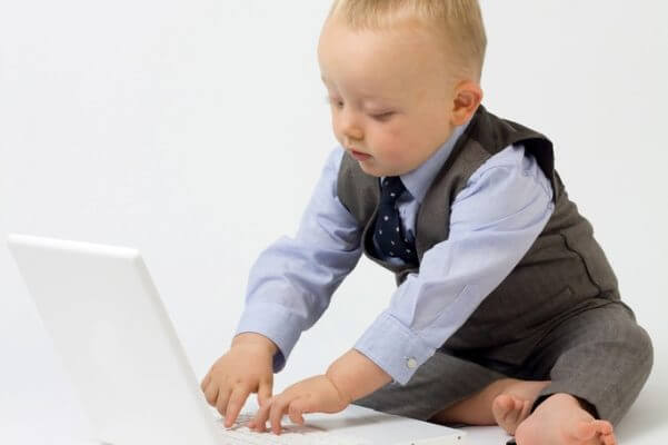 Fotografía de un bebé vestido con traje y chaleco, tecleando en un ordenador portátil, como si fuera un ejecutivo.