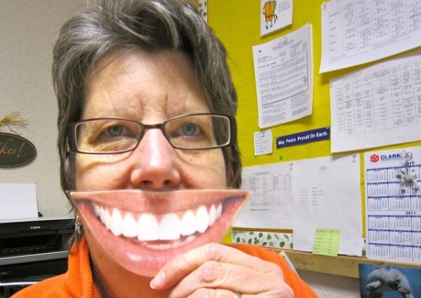 Una fotografía de una mujer que sostiene una sonrisa recortada de una fotografía ante su cara.