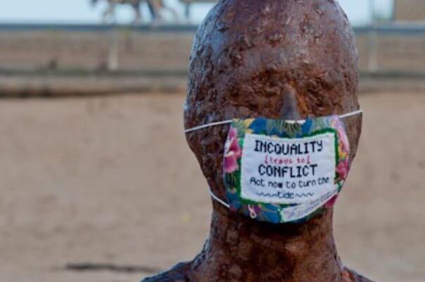 Una estatua de Antony GormLey, en la que han puesto una máscara como las de los cirujanos. Bordado en la máscara se puede leer "La desigualdad desemboca en el conflicto, actúa ahora para cambiar el rumbo", en inglés.