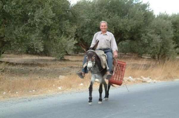 Un hombre de campo, circulando por una carretera secundaría, mientras monta su burro.