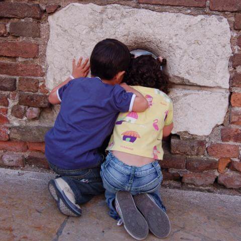 Dos niños asomandose por un agujero en la pared.