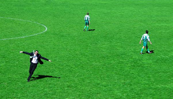 Una hombre vestido de traje, corriendo por un campo de fútbol con los brazos abiertos, en pleno juego. Como si tuviera la confianza suficiente para comerse el mundo.