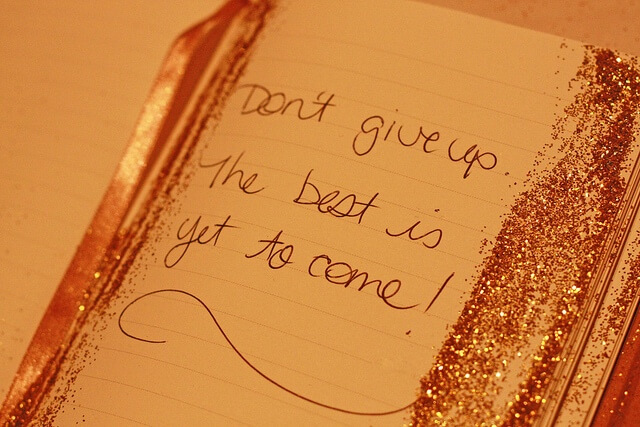 Una libreta con algo de purpurina pegada en los bordes laterales de las páginas, donde se puede leer "Don't give up. The best is yet to come!".