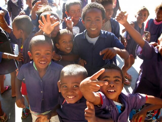 Un grupo de niños de Madagascar, vestidos con camisetas azul oscuro, mirando a la cámara y sonriendo a quienes van a tratar de proveerles de agua potable.