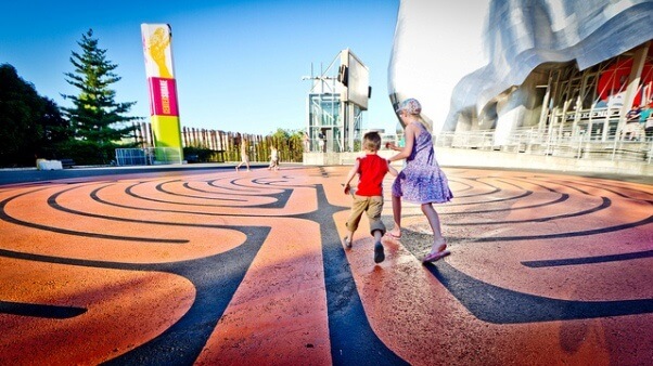 Un par de niños corriendo en una explanada llena de dibujos y colores, cercana al EMP (Experience music project Museum).