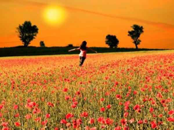 Una mujer corriendo por un campo lleno de flores, con los brazos abiertos. Mostrando una actitud que denota mucho la felicidad que llena su vida.